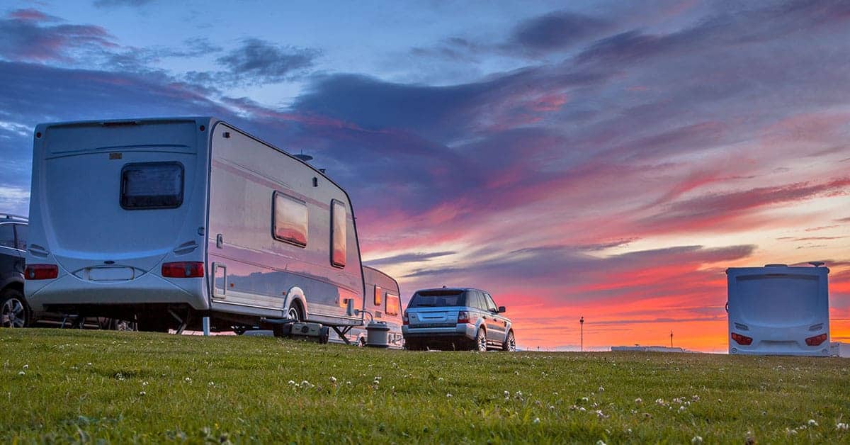 Recreational trailers parked on grass at sunset, emphasizing trailer maintenance and outdoor adventures.