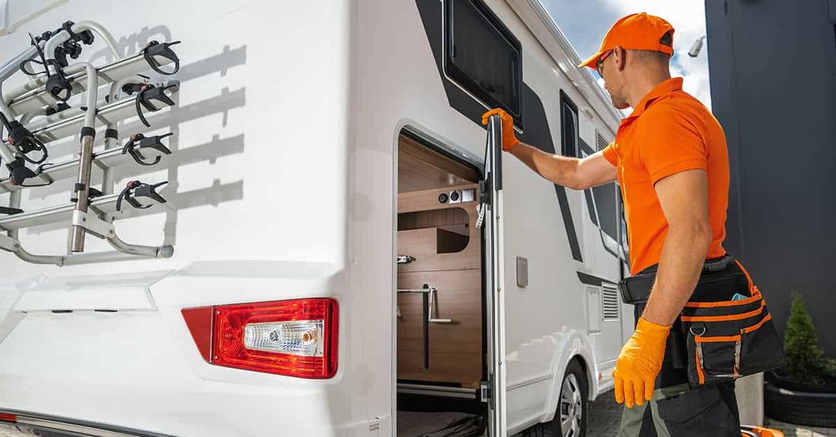 RV technician inspecting entry door of a recreational vehicle, emphasizing importance of regular RV inspections for maintenance and safety.