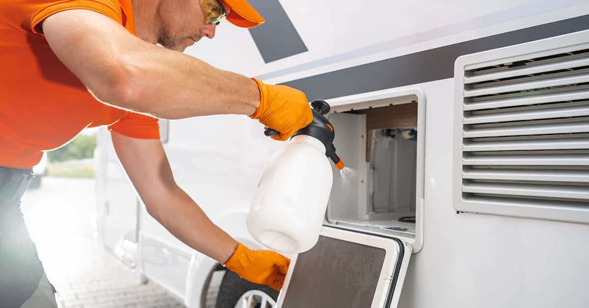 Person in orange shirt and gloves cleaning an RV with a spray bottle, focusing on maintenance tasks relevant to DIY RV care.