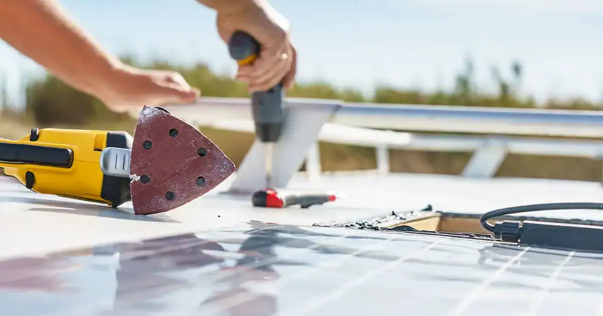 Hands using power tools on an RV roof, demonstrating maintenance and repair techniques for RV roof replacement options.
