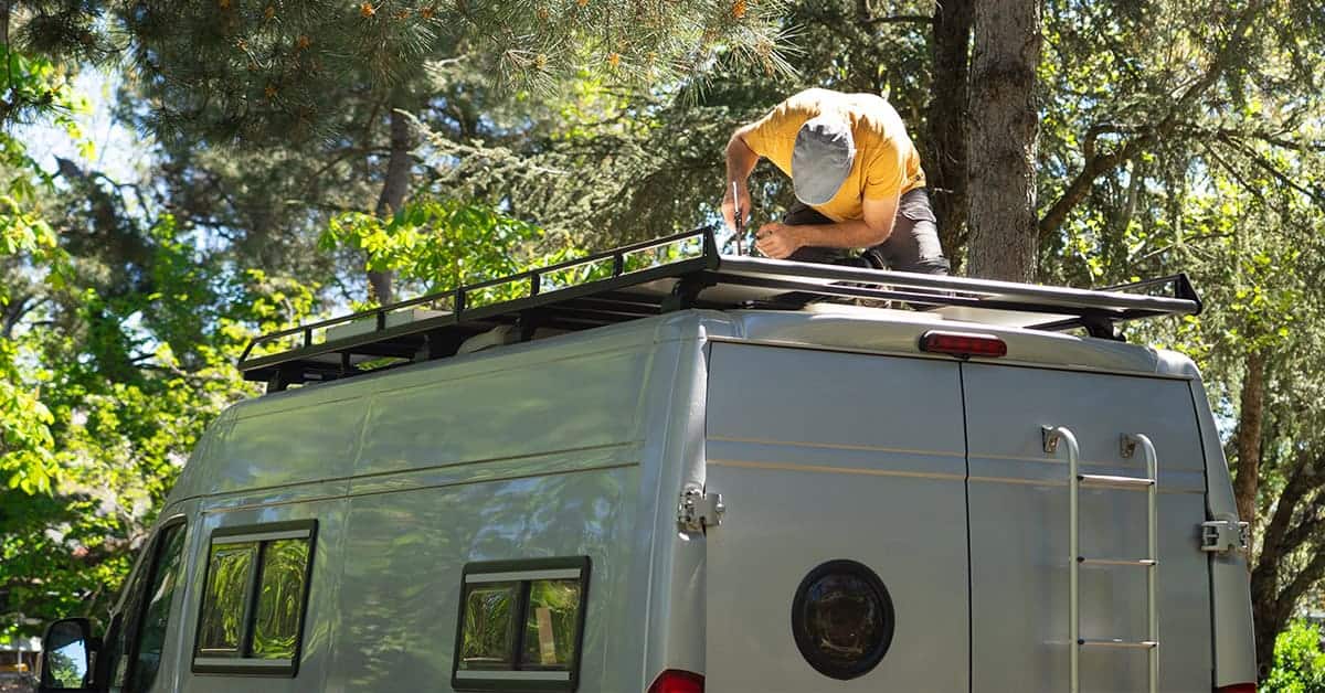 Person inspecting and repairing an RV roof in a lush outdoor setting, emphasizing RV maintenance for spring travel readiness.