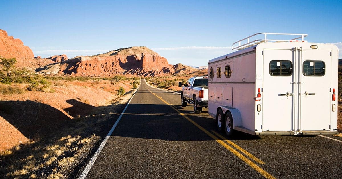 White trailer being towed by a pickup truck on a scenic road surrounded by red rock formations, emphasizing the importance of trailer maintenance and safety.