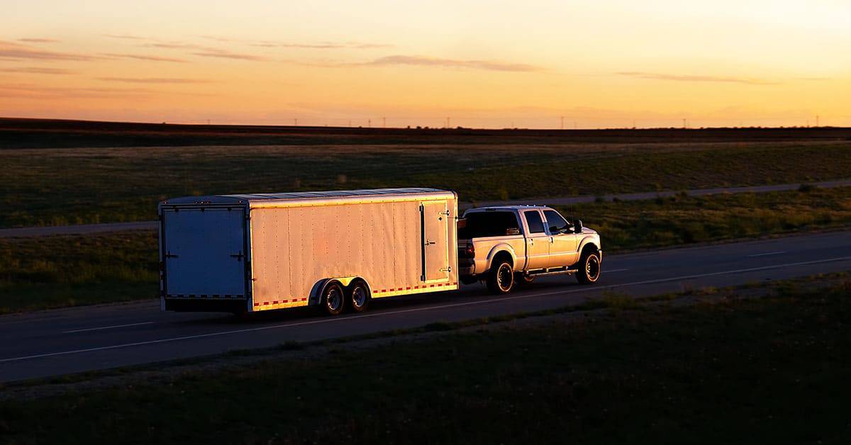 Truck towing an enclosed trailer on a highway at sunset, illustrating trailer usage and maintenance relevance.